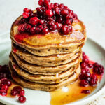 A stack of American-style pancakes topped with lingonberries and syrup.