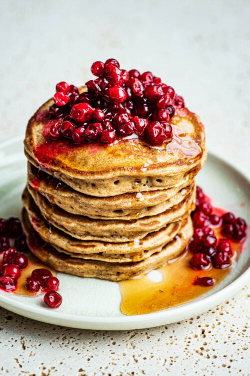 A stack of American-style pancakes topped with lingonberries and syrup.
