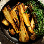 Golden honey roasted parsnips in a deep plate with thyme on the side.