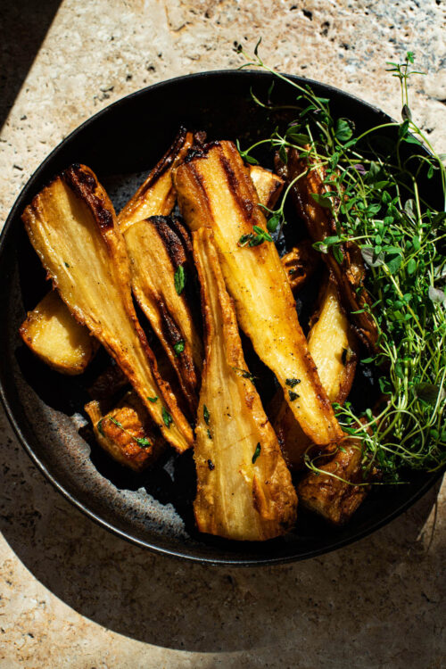 Golden honey roasted parsnips in a deep plate with thyme on the side.