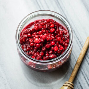 Lingonberry sauce in a glass jar with a honey dipper in front.