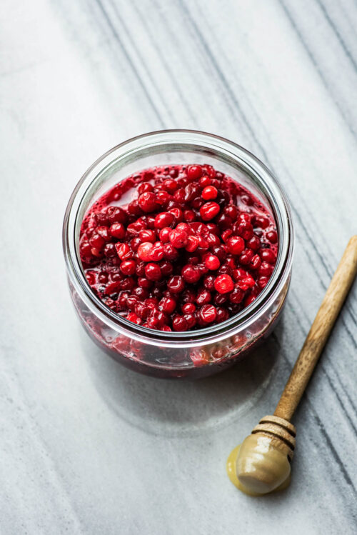 Lingonberry sauce in a glass jar with a honey dipper in front.