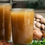 Two jars of broth with mushrooms around.