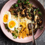 A bowl of porridge topped with mushrooms, herbs, preserved lemon, and a boiled egg.