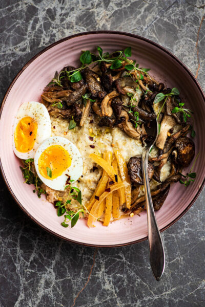 A bowl of porridge topped with mushrooms, herbs, preserved lemon, and a boiled egg.