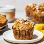 Oat-topped muffin on a small plate with more muffins behind.