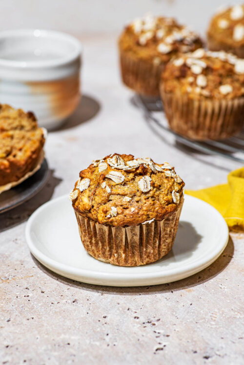 Oat-topped muffin on a small plate with more muffins behind.