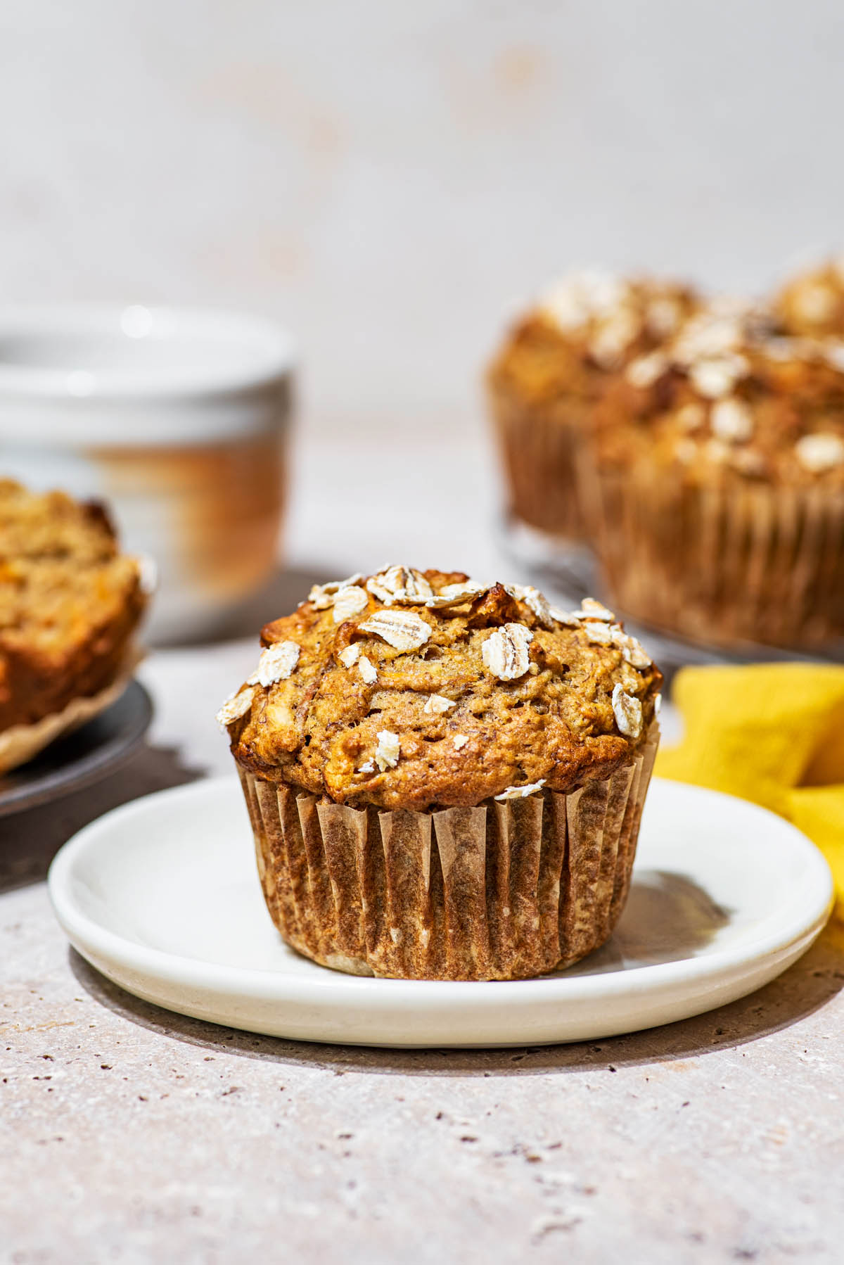 Oat-topped muffin on a small plate with more muffins behind.