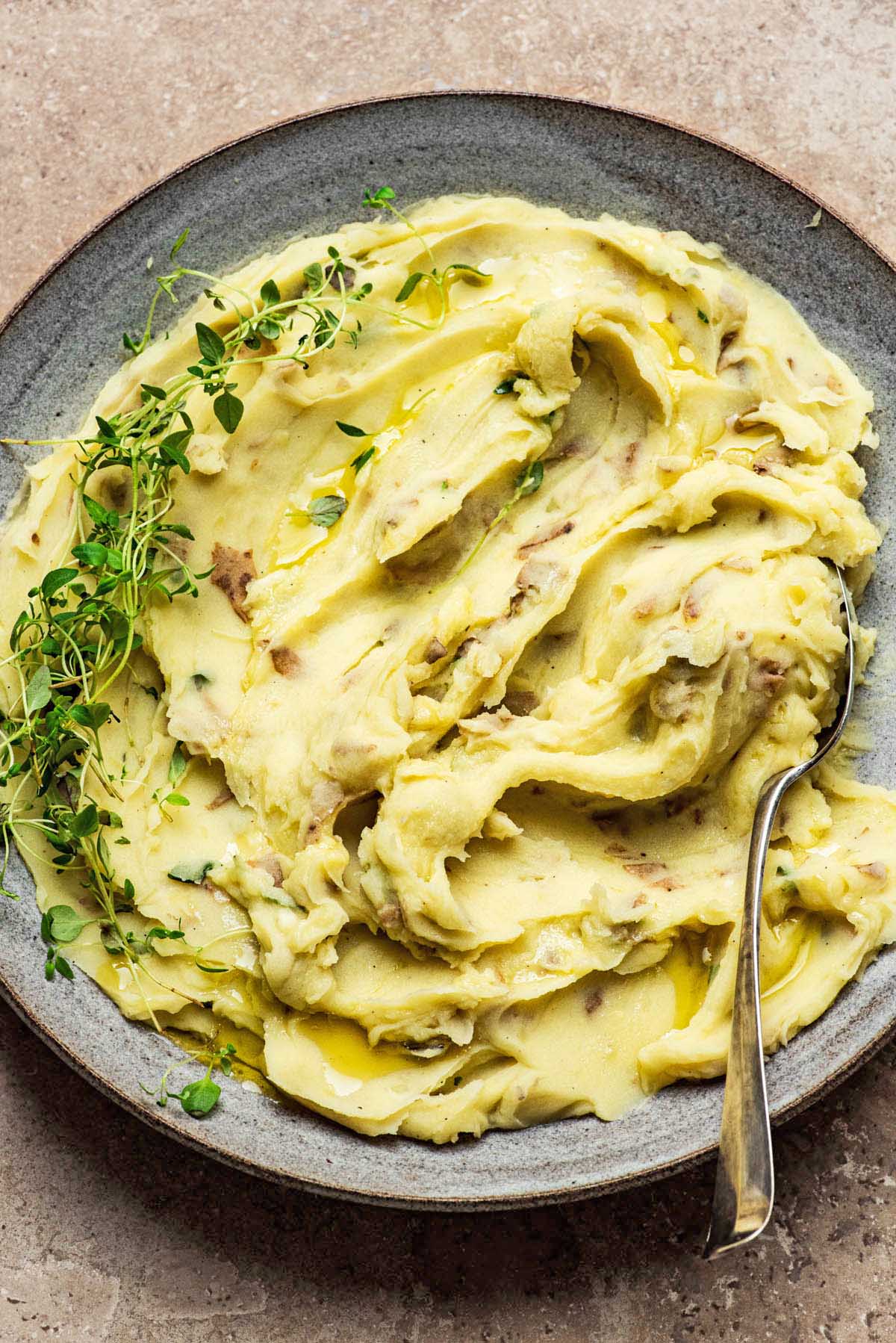 A bowl of creamy mashed potatoes with thyme.