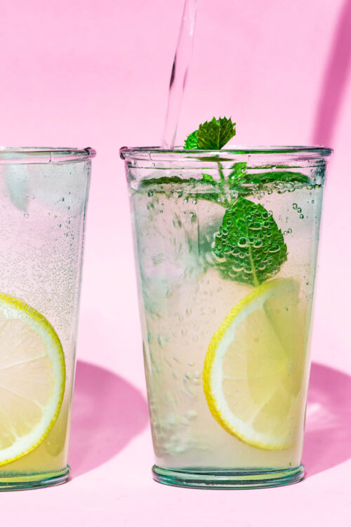 Close up of sparkling water being poured into a glass of mint lemonade.