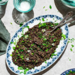 Lentil salad on a platter with chopped herbs and garlic mustard flowers.