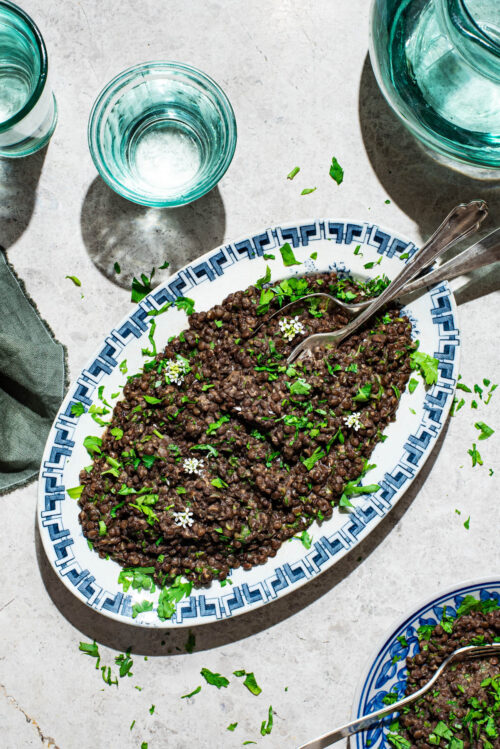 Lentil salad on a platter with chopped herbs and garlic mustard flowers.
