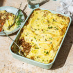 A lentil cottage pie in a rectangular baking dish, with one scoop removed to see the filling under the mashed potatoes.