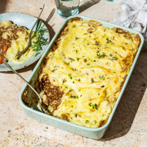A lentil cottage pie in a rectangular baking dish, with one scoop removed to see the filling under the mashed potatoes.