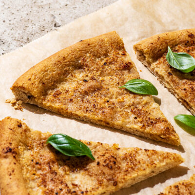 Slices of baked garlic pizza dough cut into triangles, with fresh basil leaves.