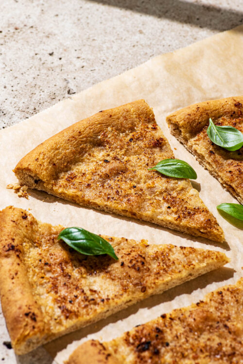 Slices of baked garlic pizza dough cut into triangles, with fresh basil leaves.