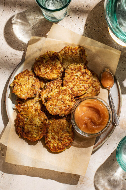 A plate of potato pancakes with a jar of applesauce.