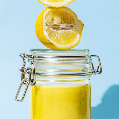 A glass jar filled with lemon vinaigrette, two lemon pieces sitting on the lid.