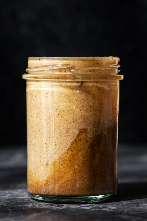 A glass jar, front view, filled with a tahini dressing.