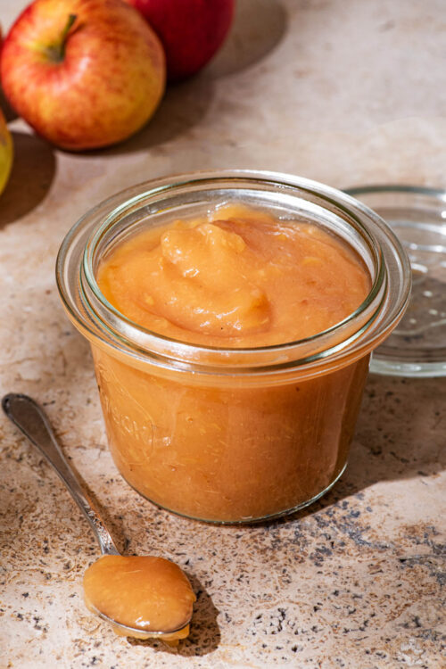 A glass canning jar filled with applesauce, apples in the background.