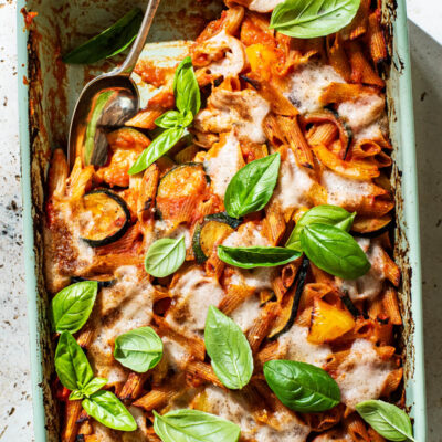 Baked penne pasta in a casserole dish with tomato sauce, vegetables, and cheese.