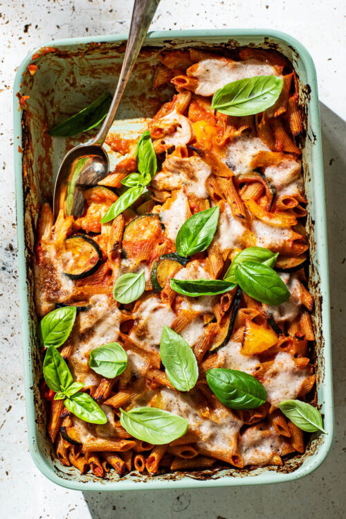 Baked penne pasta in a casserole dish with tomato sauce, vegetables, and cheese.