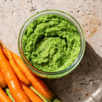 Carrot top pesto in a glass jar with fresh carrots beside it.