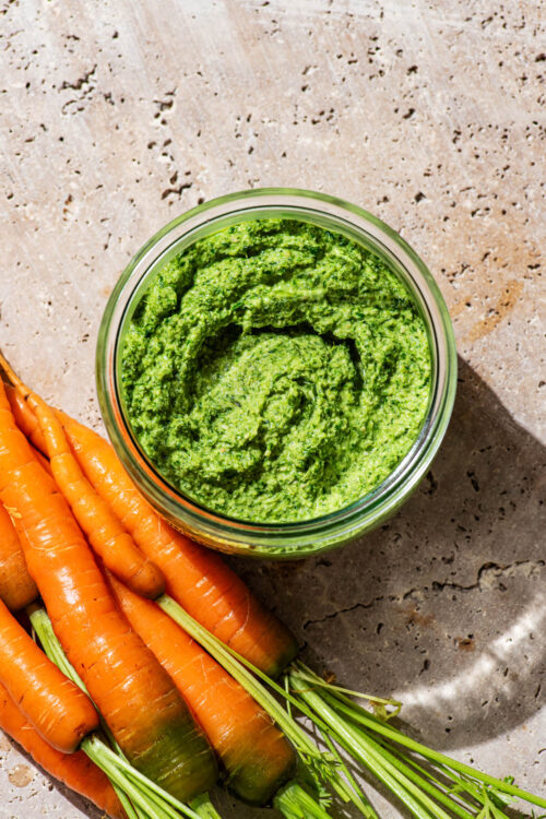 Carrot top pesto in a glass jar with fresh carrots beside it.