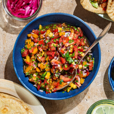 A bowl of fresh salsa surrounded by tacos, tortillas, and other toppings.