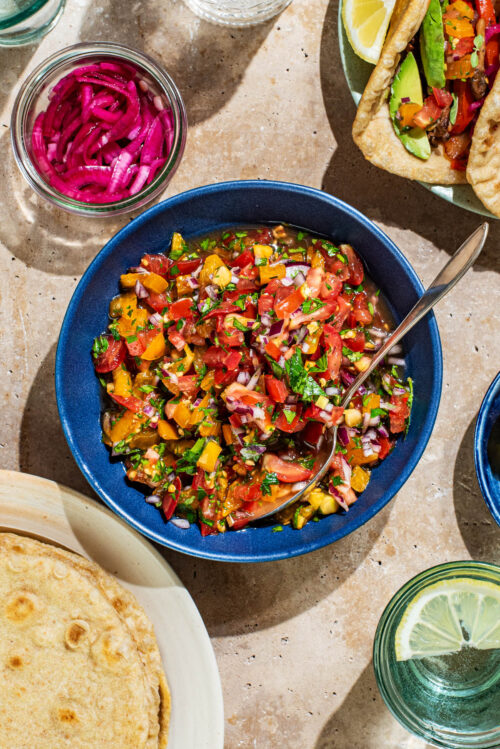 A bowl of fresh salsa surrounded by tacos, tortillas, and other toppings.