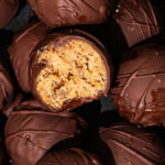 Close up of chocolate-coated peanut butter balls, one halved to show interior.