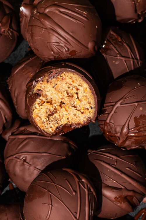 Close up of chocolate-coated peanut butter balls, one halved to show interior.
