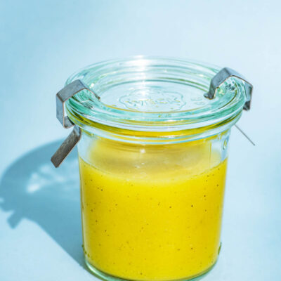 Vinaigrette in a small glass jar with a lid on a blue background.