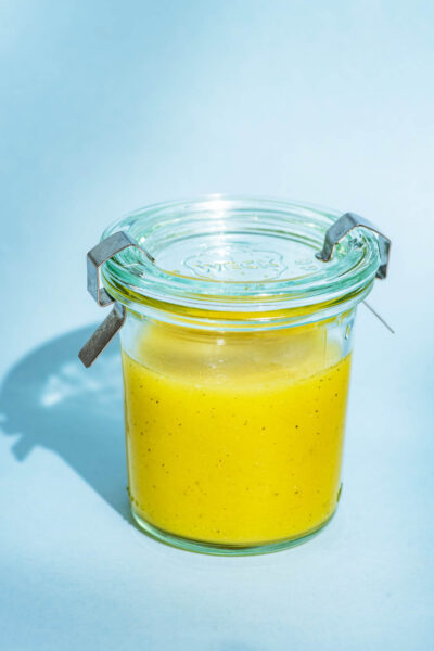 Vinaigrette in a small glass jar with a lid on a blue background.