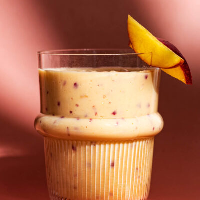 Close up of a smoothie in a glass on a pink background, with two slices of nectarine.