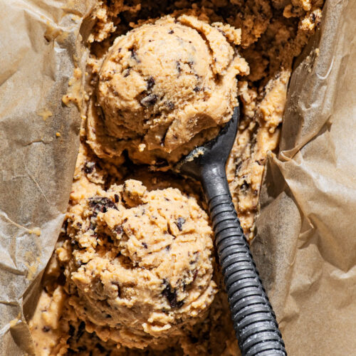 Two scoops of ice cream in a lined loaf tin with a ice cream scooper in the tin.