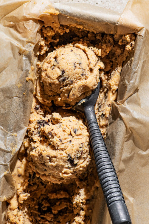 Two scoops of ice cream in a lined loaf tin with a ice cream scooper in the tin.