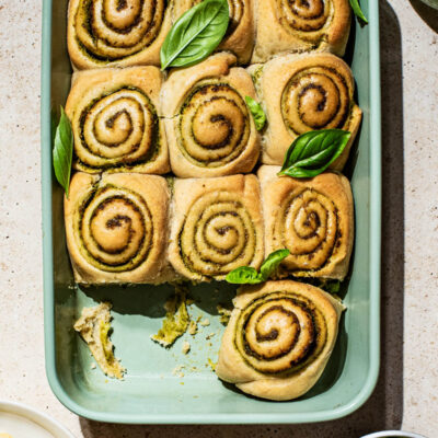 Pesto filled rolls in a green baking dish with basil leaves.
