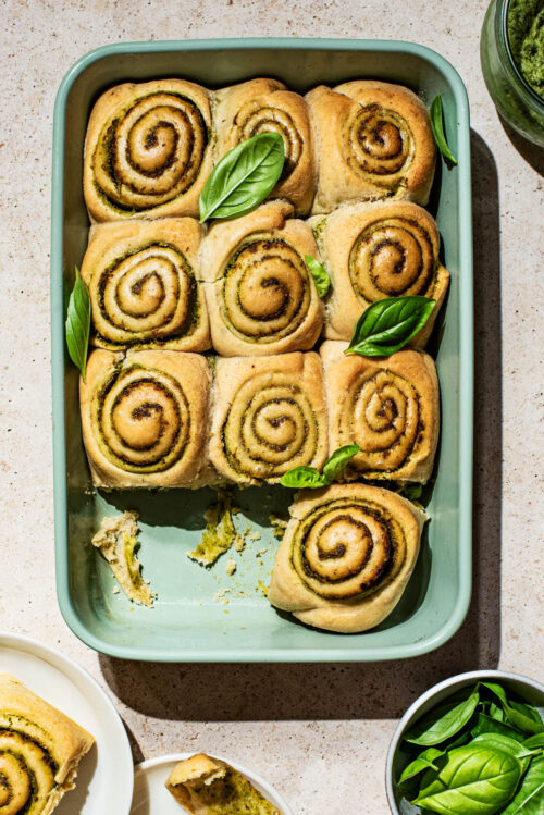 Pesto filled rolls in a green baking dish with basil leaves.