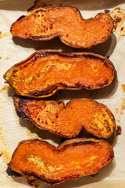 Roasted sweet potatoes cut-side up in hard light.