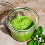 Pesto in a glass jar with rocket leaves beside it.