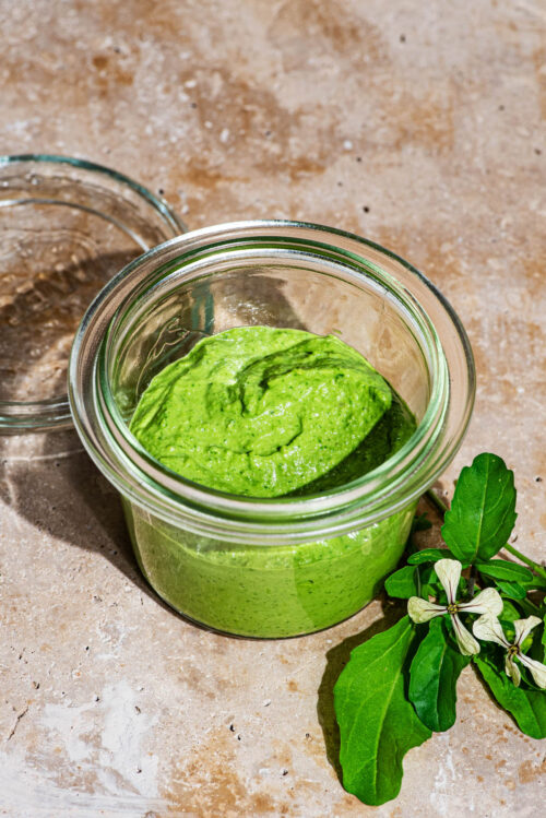 Pesto in a glass jar with rocket leaves beside it.