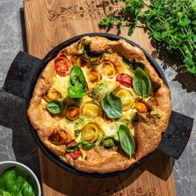 A puffy baked pancake in a cast iron pan with small tomatoes and basil.