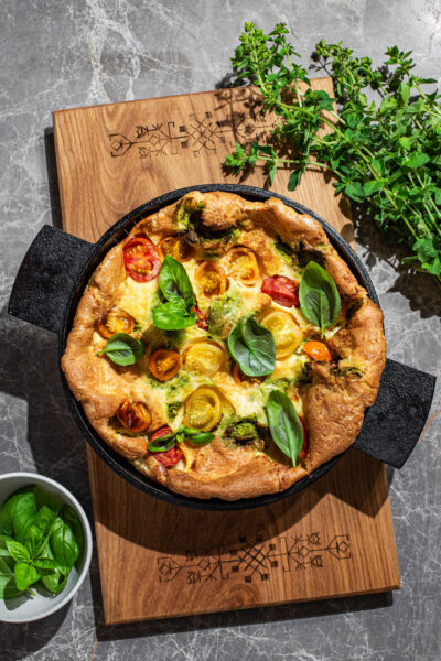A puffy baked pancake in a cast iron pan with small tomatoes and basil.