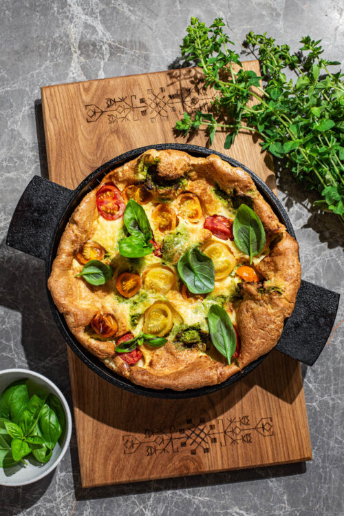 A puffy baked pancake in a cast iron pan with small tomatoes and basil.