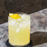 A single glass of lemonade with ice and a lemon peel in a crystal glass.