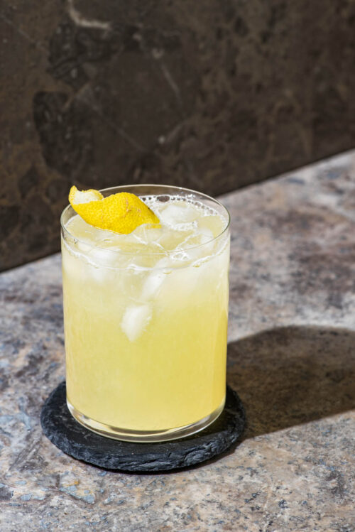 A single glass of lemonade with ice and a lemon peel in a crystal glass.