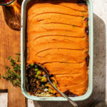 A lentil pie topped with sweet potato mash, one serving removed from the baking dish.