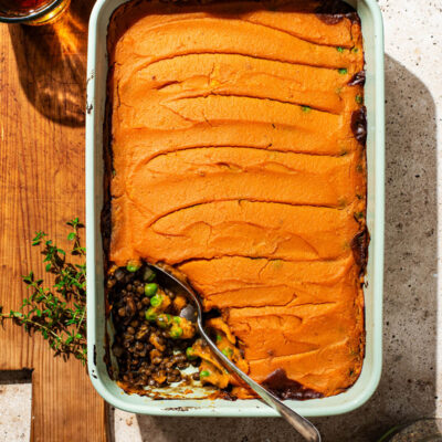 A lentil pie topped with sweet potato mash, one serving removed from the baking dish.