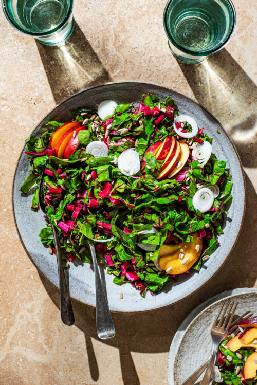A chard salad with sliced nectarine, onion, and sunflower seeds in direct light.